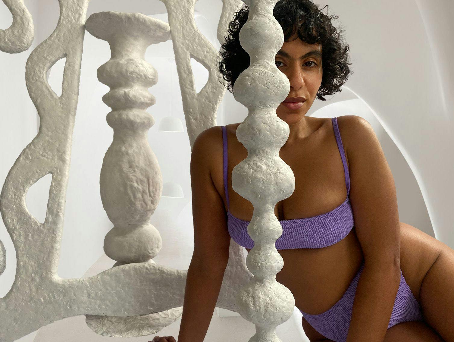 Nadine sitting with one of her sculptures, wearing a lilac bikini